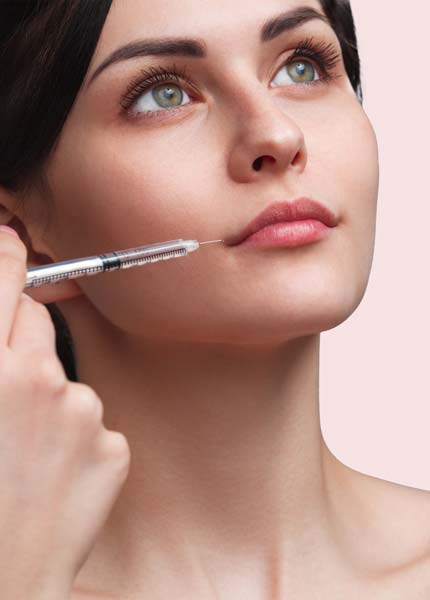 Eine Frau mit schwarzen Haaren blickt schräg nach oben. Vor ihrem Gesicht sieht man eine Spritze in der Nähe ihrer Lippen.