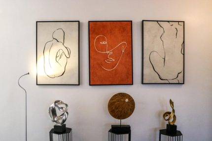 Drei Bilder mit grafischen Darstellungen an einer Wand. Unter den Bildern stehen drei moderne Skulpturen.