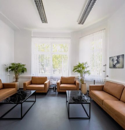 Ein Warteraum des Care Cute Schönheitsinstituts, in dem mehrere braune Ledermöbel und Couchtische aus Glas stehen.